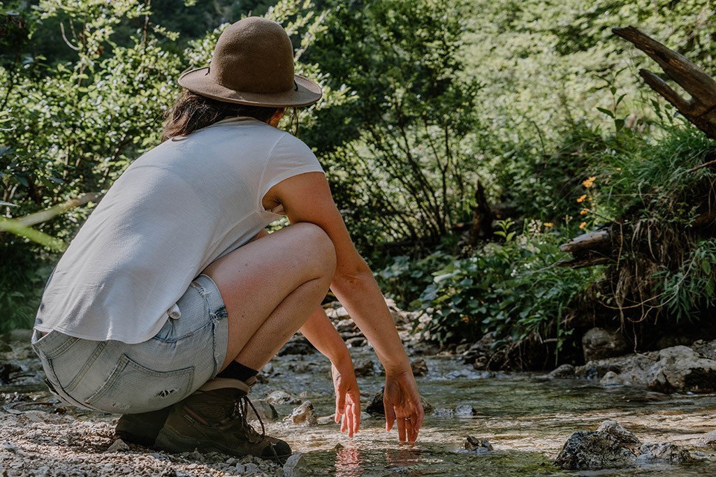 Person hockt an Wasser und trägt Mojak Hut