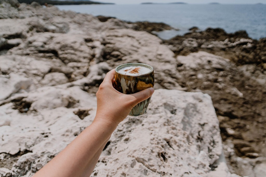 Person hält getöpferten Becher mit Milchschaum in der Hand.