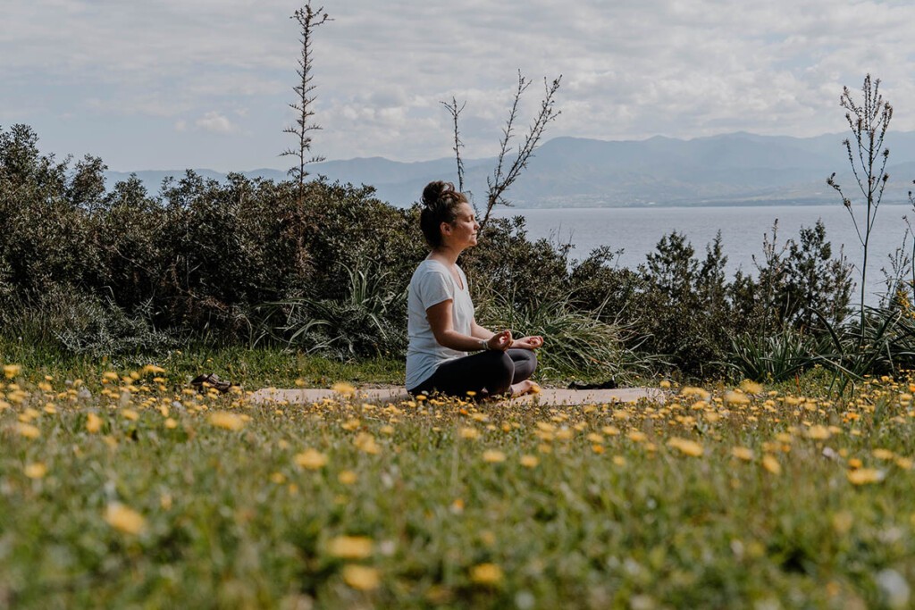 Person meditiert auf Yogamatte auf Blumenwiese.