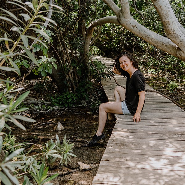 Elisa Model vom Camping Blog take an adVANture trägt ein schwarzes Oberteil und eine kurze Jeanshose, sie sitzt dabei auf einem Steg und blickt in die Kamera.