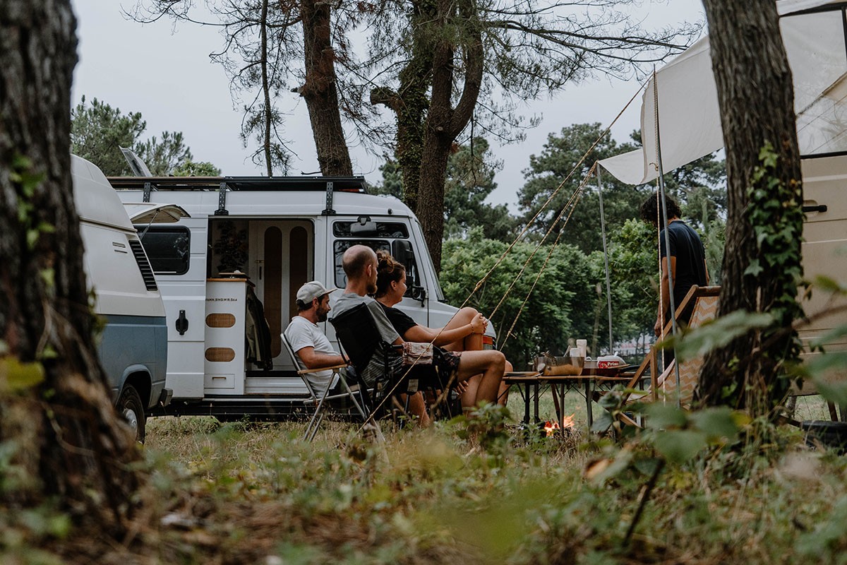 Zeit statt Zeug verschenken: Mehrere Personen sitzen zwischen ihren Campingfahrzeugen im Grünen.