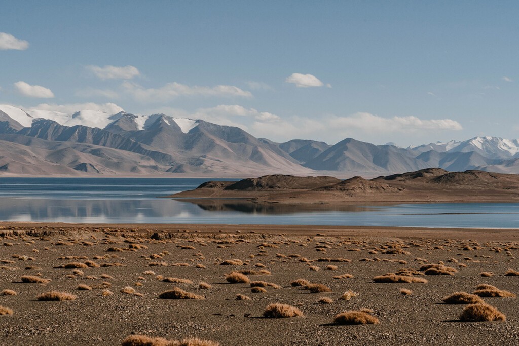 Blick auf den Karakul See in Tadschikistan. Wasser leuchtet Blau, im Hintergrund befinden sich die schneebedeckten Berge vom Pamir-Gebirge.