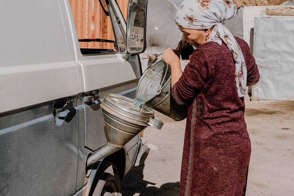 Frau betankt VW T3 Camper in Murghab mit Trichter und Eimer.