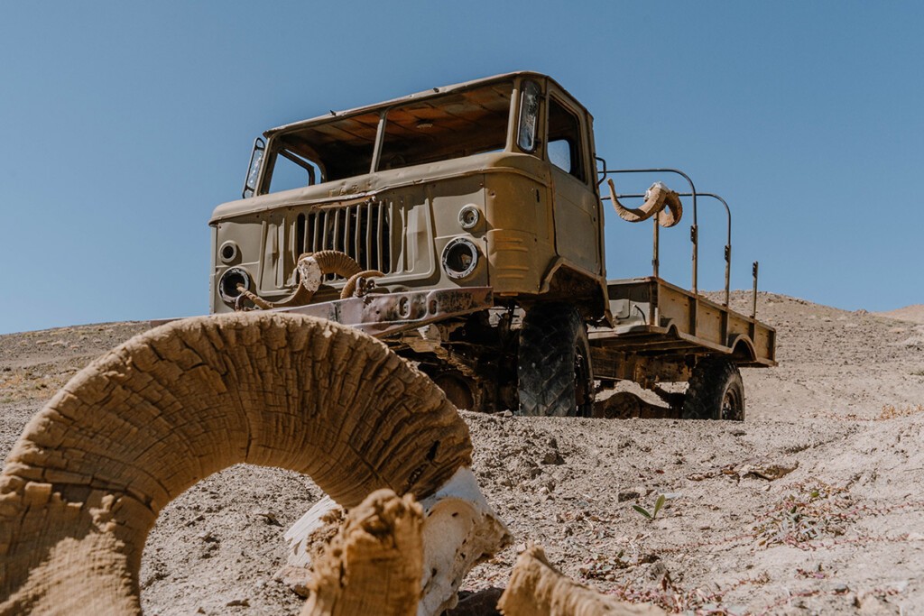 Alter, verrosteter LKW, ausgeschlachtet, steht auf Schotter. Davor liegen die Hörner eines Pamir-Argali, dem Marco-Polo-Schaf.