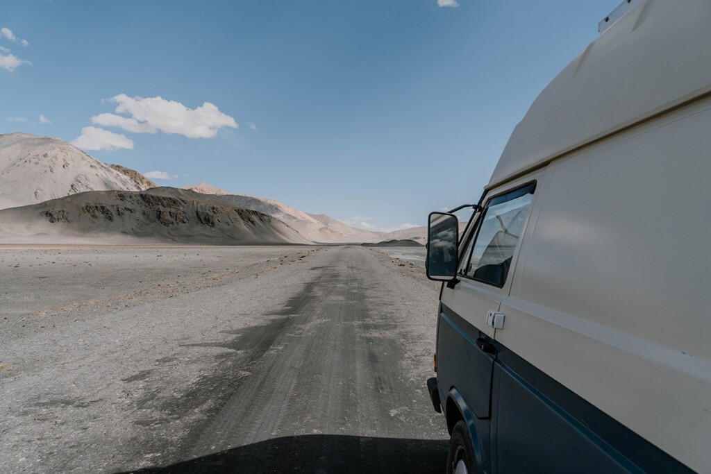 VW T3 Camper steht auf Pamir-Highway, der bis zum Horizont gerläuft.