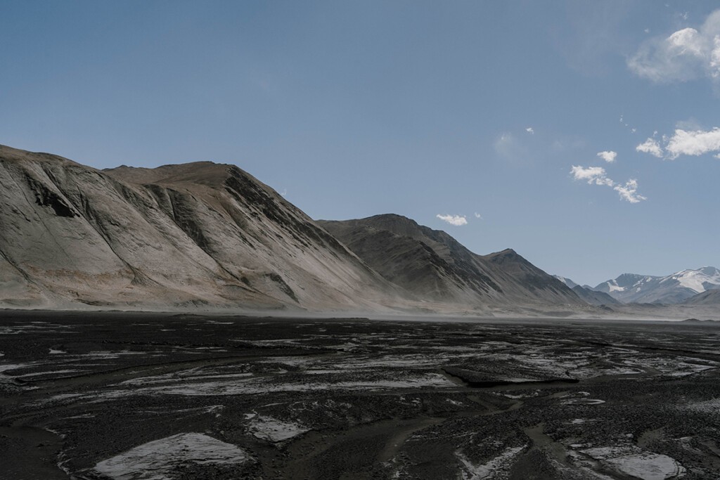 Schwarzes, ausgetrocknetes Flussbett mit grauen Bergen im Hintergrund.