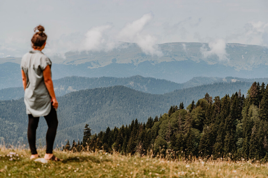 Elisa Model von take an adVANture steht im Kleinen Kaukasus auf einer Wiese und blickt über die weite, bergige Landschaft.