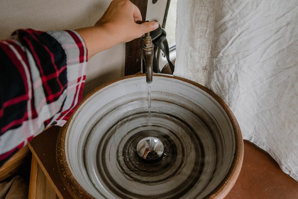 Person öffnet Wasserhahn in einem Camper, Wasser fließt in ein Waschbecken aus Ton.