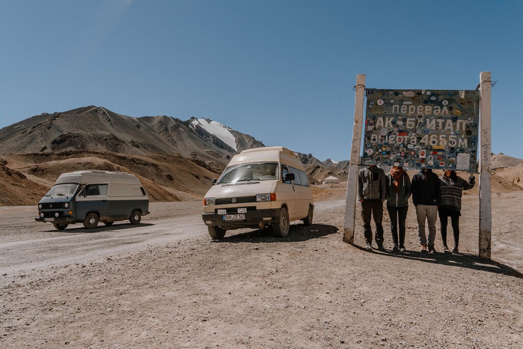 Zwei VW Camper und vier Personen stehen am Schild vom Pamir-Highway Ak-Baital-Pass in Tadschikistan.