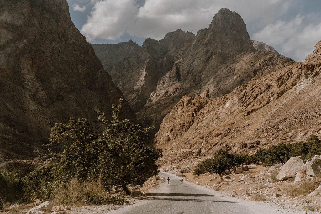 Pamir-Highway verläuft zwischen Bergflanken, auf der Straße laufen zwei junge Männer.