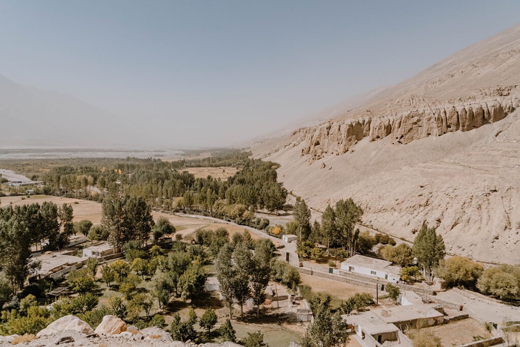 Blick über das Wakhan Valley von oberhalb, mit weißen Häusern, grünen Bäumen, sandiger Luft.
