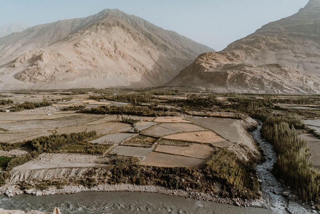 Blick auf die afghanische Seite im Wakhan Valley, mit Feldern, grünen Wiesen und einem Flusslauf zwischen den Bergen.
