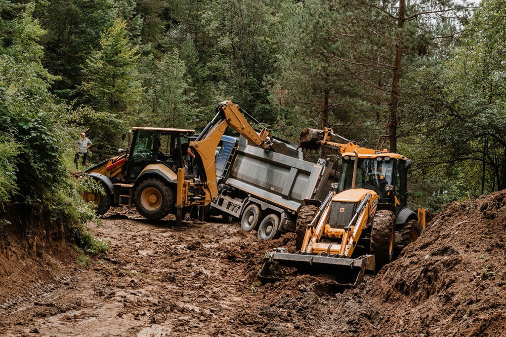 Matschige Passstraße im Wald, zwei Traktoren versuchen einen LKW zu bergen. Die Beachtung der Straßenverhältnisse der Nebenstraße gehört zu einem wichtigen Georgien Reisetipp.