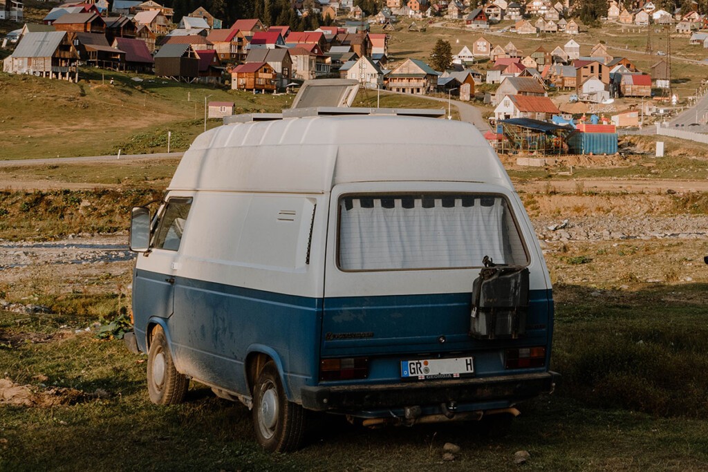 VW T3 Camper steht auf Wiese im Kleinen Kaukasus, im Hintergrund sieht man dörfliche Bebauung.