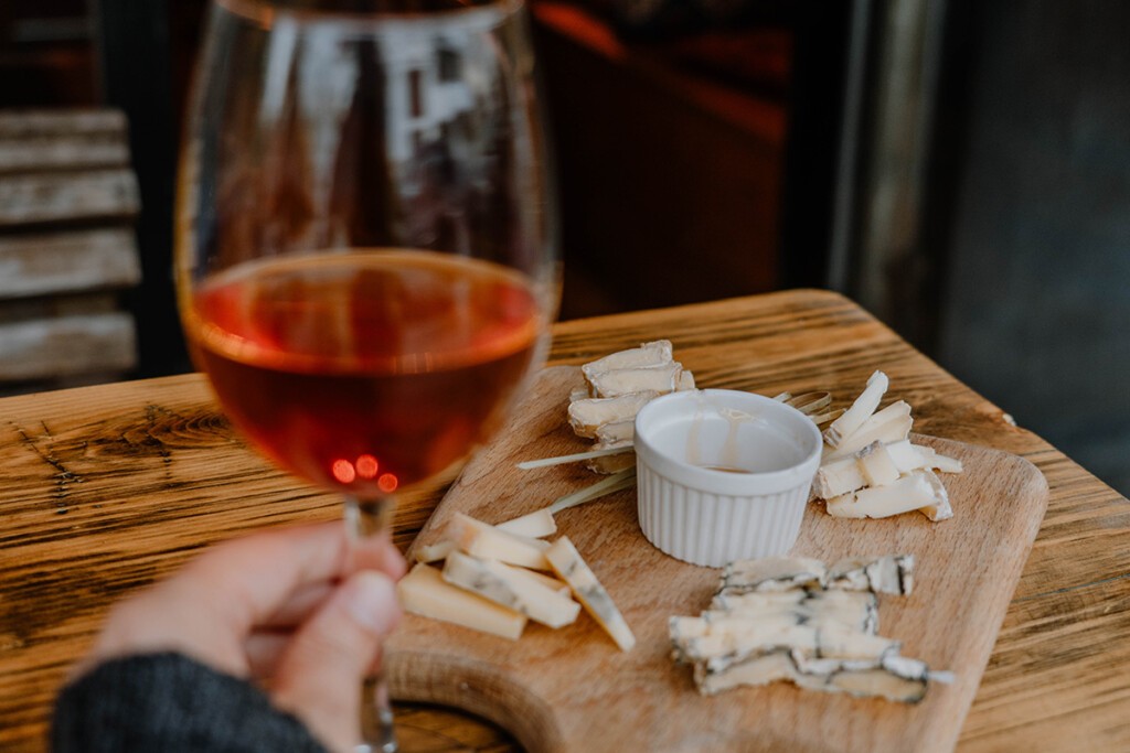 Georgien Reisetipp kulinarisch: Person hält Glas mit georgischem Wein in der Hand, im Hintergrund steht eine Käseplatte.