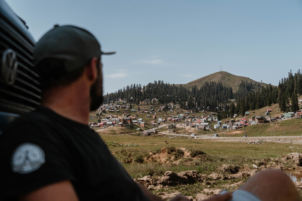 Reise nach Georgien: Camper sitz vor seinem VW T3 und blickt in die Ferne auf ein Dorf am Berghang.