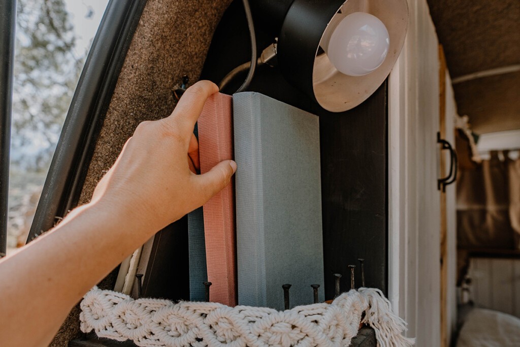 Person nimmt Buch aus Regal in VW T5 Camper.