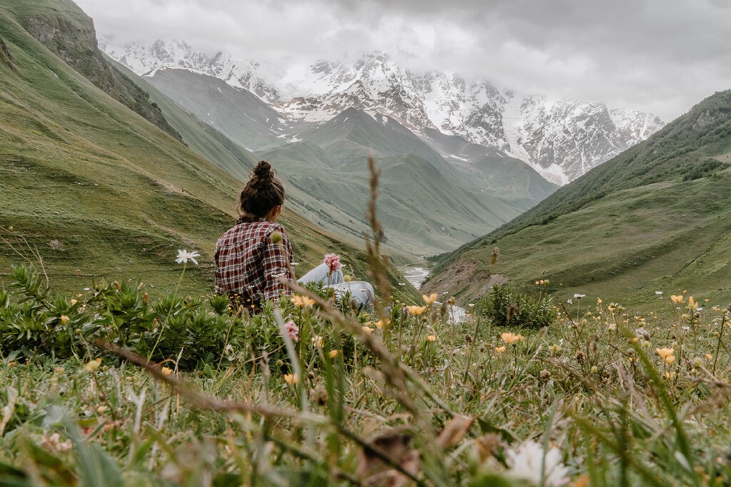 Elisa Model vom Camping Blog take an adVANture sitzt auf Wiese in Georgien und blickt Richtung Berge.