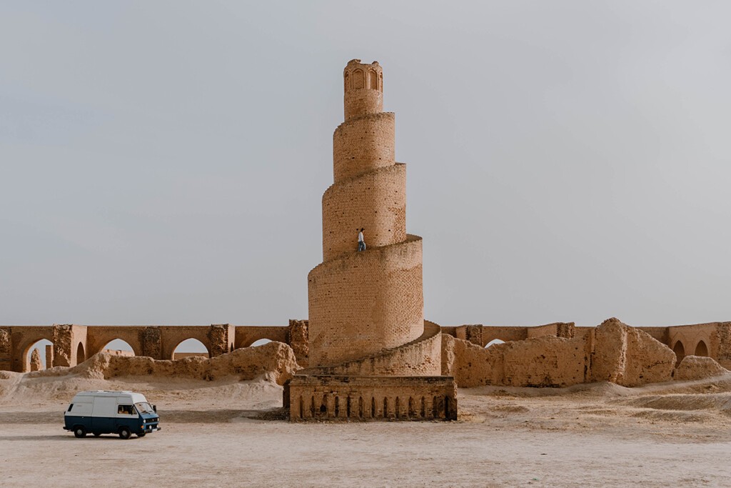 VW T3 Camper steht an altem Minarett aus Lehm im Irak.