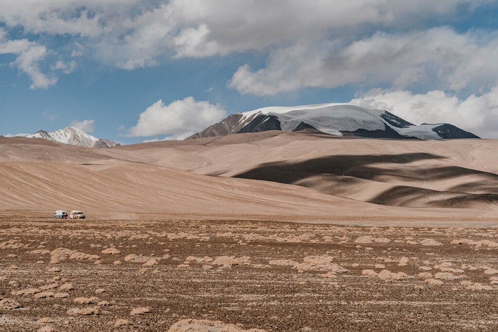Zwei VW Camper stehen am Fuße schneebedeckter Berge am Pamir-Highway in Tadschikistan.