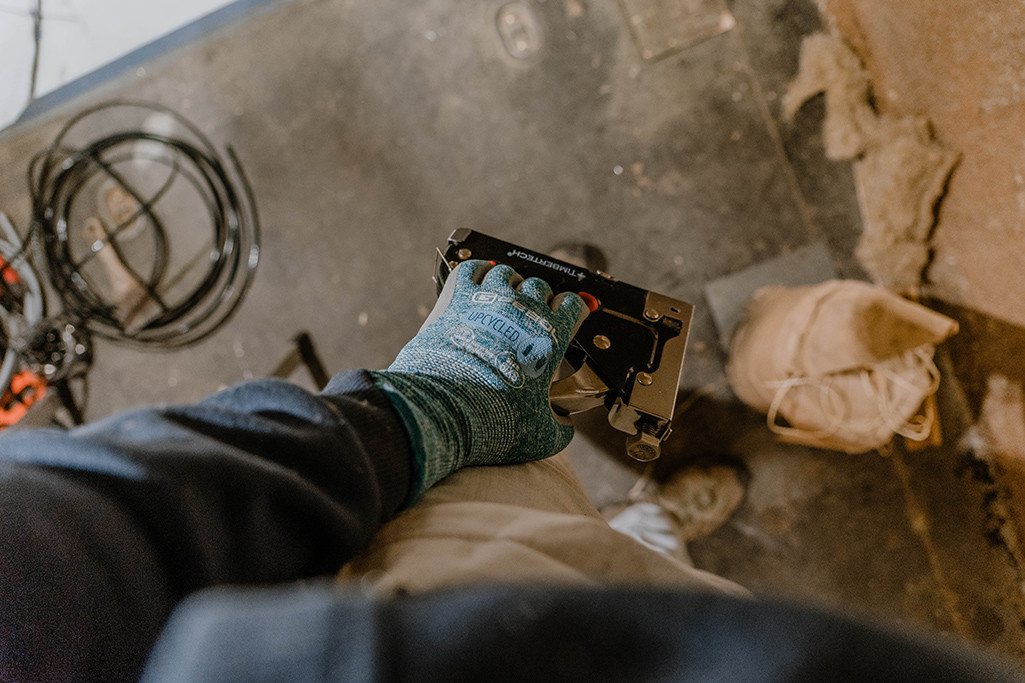 Person trägt ungecycelte Arbeitshandschuhe und hält Tacker in der Hand.