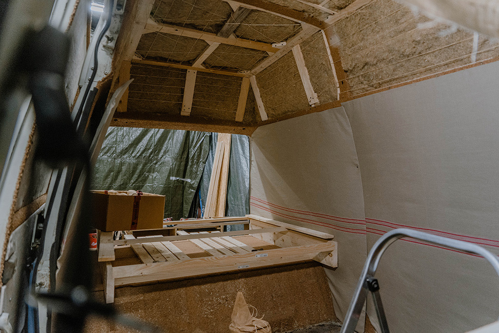 Mit Seilen an einer Unterkonstruktion gesicherte Hanfdämmung an der Decke vom Wohnmobil, seitlich von der Schiebetür aus fotografiert.