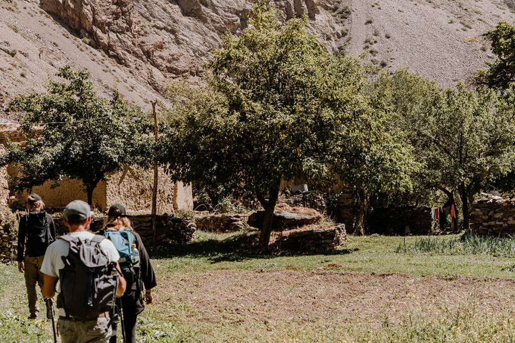 Drei Menschen wandern in das Bergdorf Jizev. Man sieht Lehmhäuser und Obstbäume.