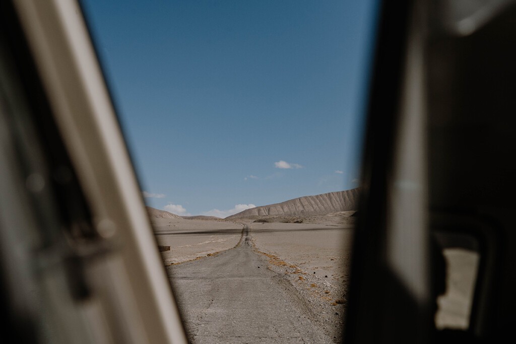 Blick aus Bulli auf gerade Straßenführung vom Pamir-Highway, der am Horizont in einer Kurve verschwindet.