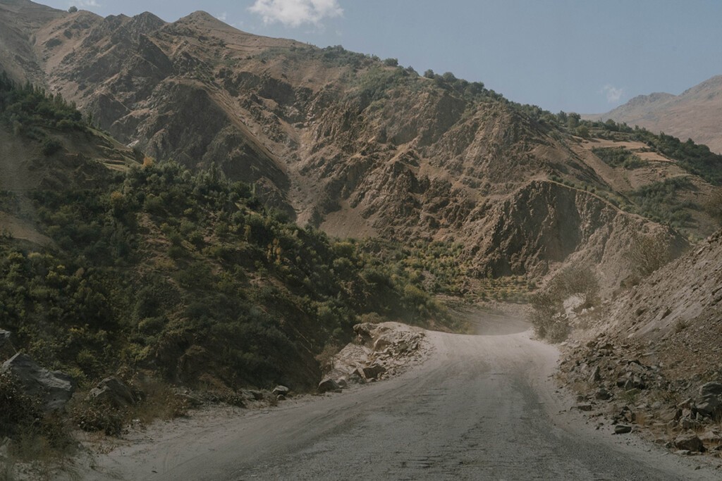 Blick auf den Pamir-Highway aus der Frontscheibe, links erstrecken sich grün bewachsene Hänge in Afghanistan.