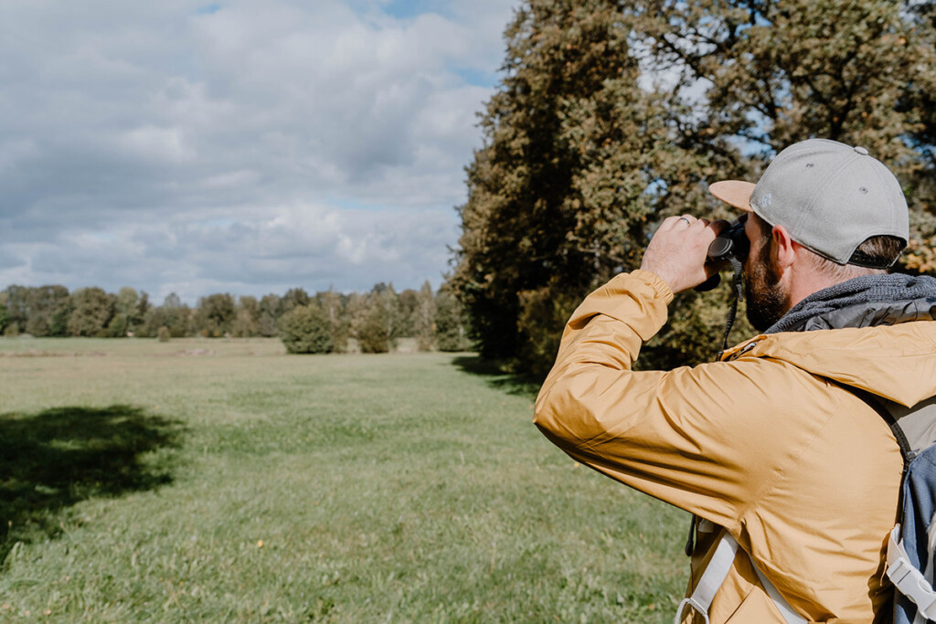 Wanderung auf dem Naturerlebnispfad Guttauer Teiche & Olbasee, Person in gelber Jacke schaut mit dem Fernglas in die Ferne.