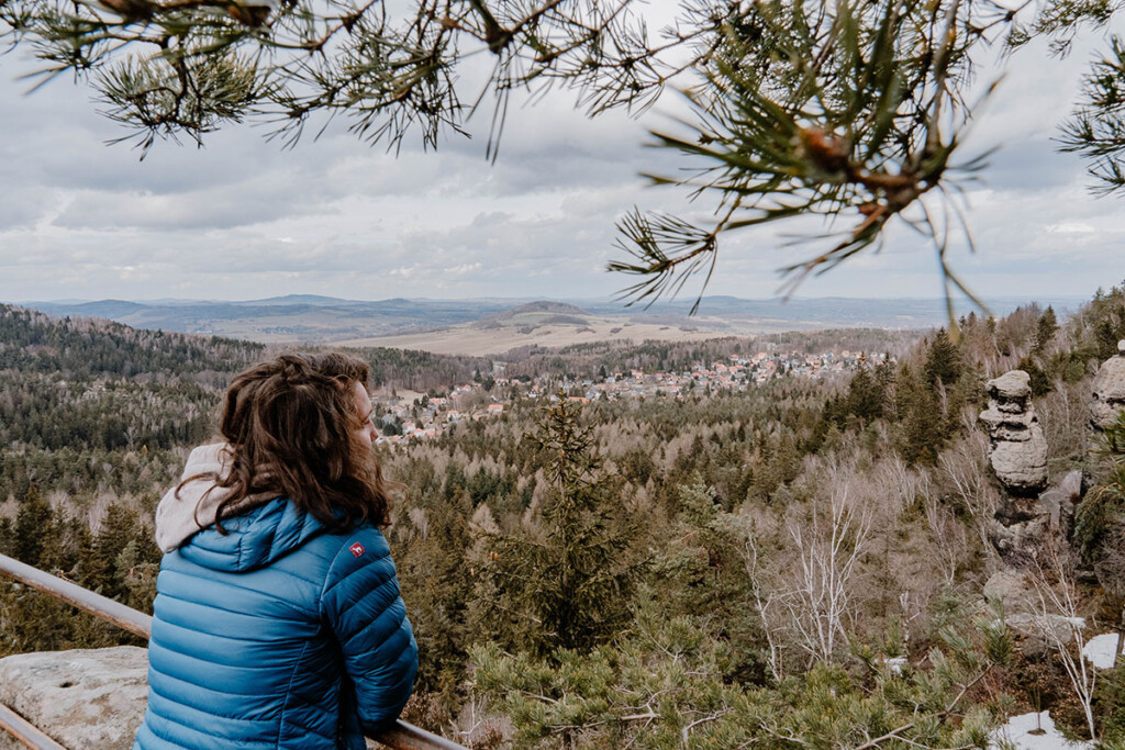 Camping Oberlausitz Tipp: Wandern im Zittauer Gebirge. Wanderin lehnt über Brüstung und schaut in die Ferne, sie trägt eine blaue Daunenjacke.