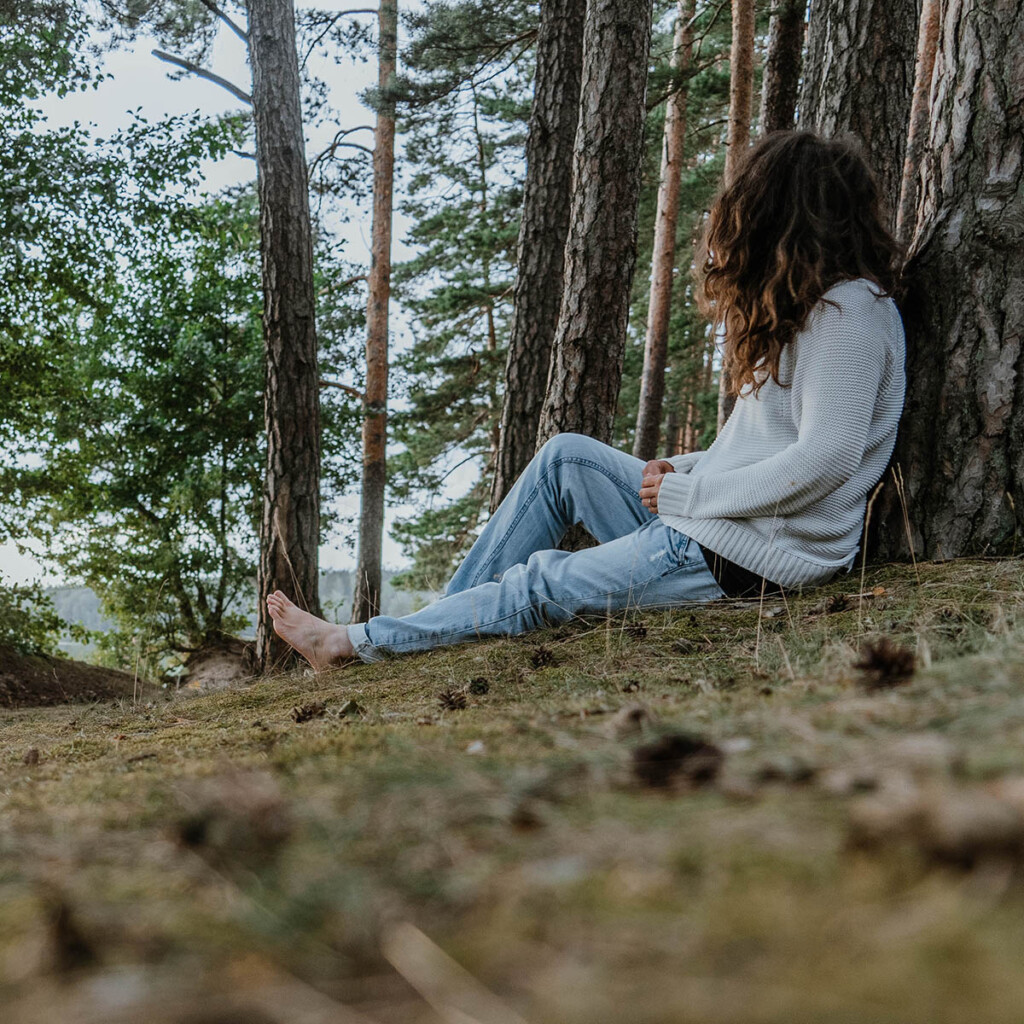 Elisa Model vom Camping Blog take an adVANture sitzt in Wald an Baum und blickt in die Ferne.