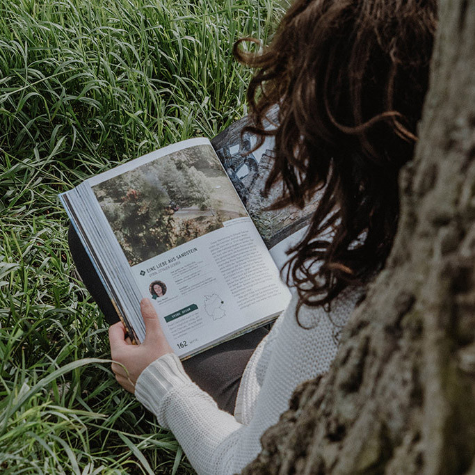 Elisa Model vom Camping Blog take an adVANture sitzt an Baum gelehnt und liest Buch.