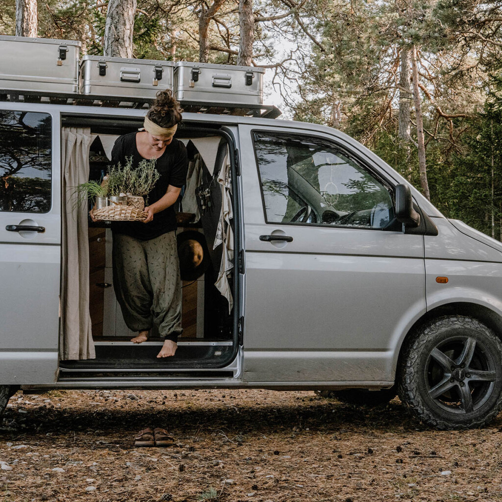Elisa Model vom Camping Blog take an adVANture steigt aus VW T5 Camper und hält Kräuterpflanzen in ihren Händen.