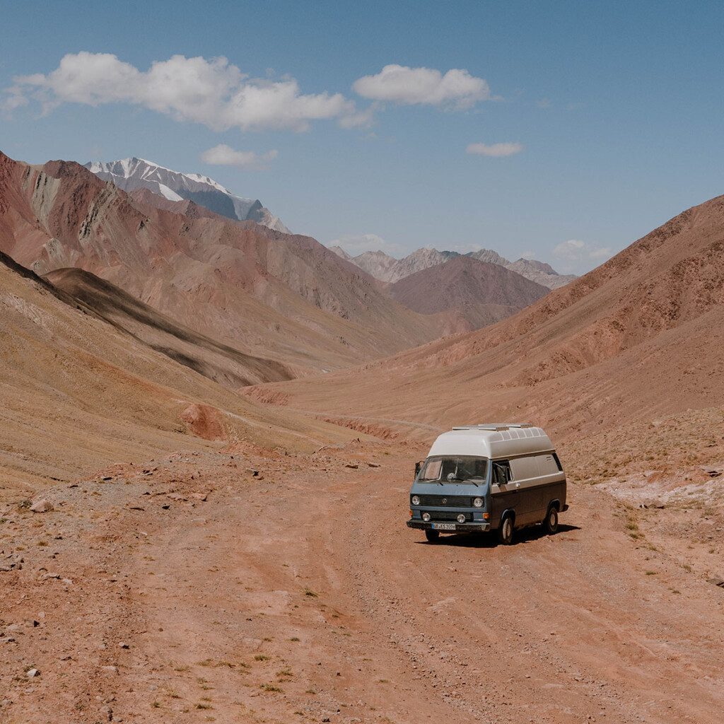 VW T3 Camper steht auf Schotterpiste zwischen Bergwelten im Pamir-Gebirge.